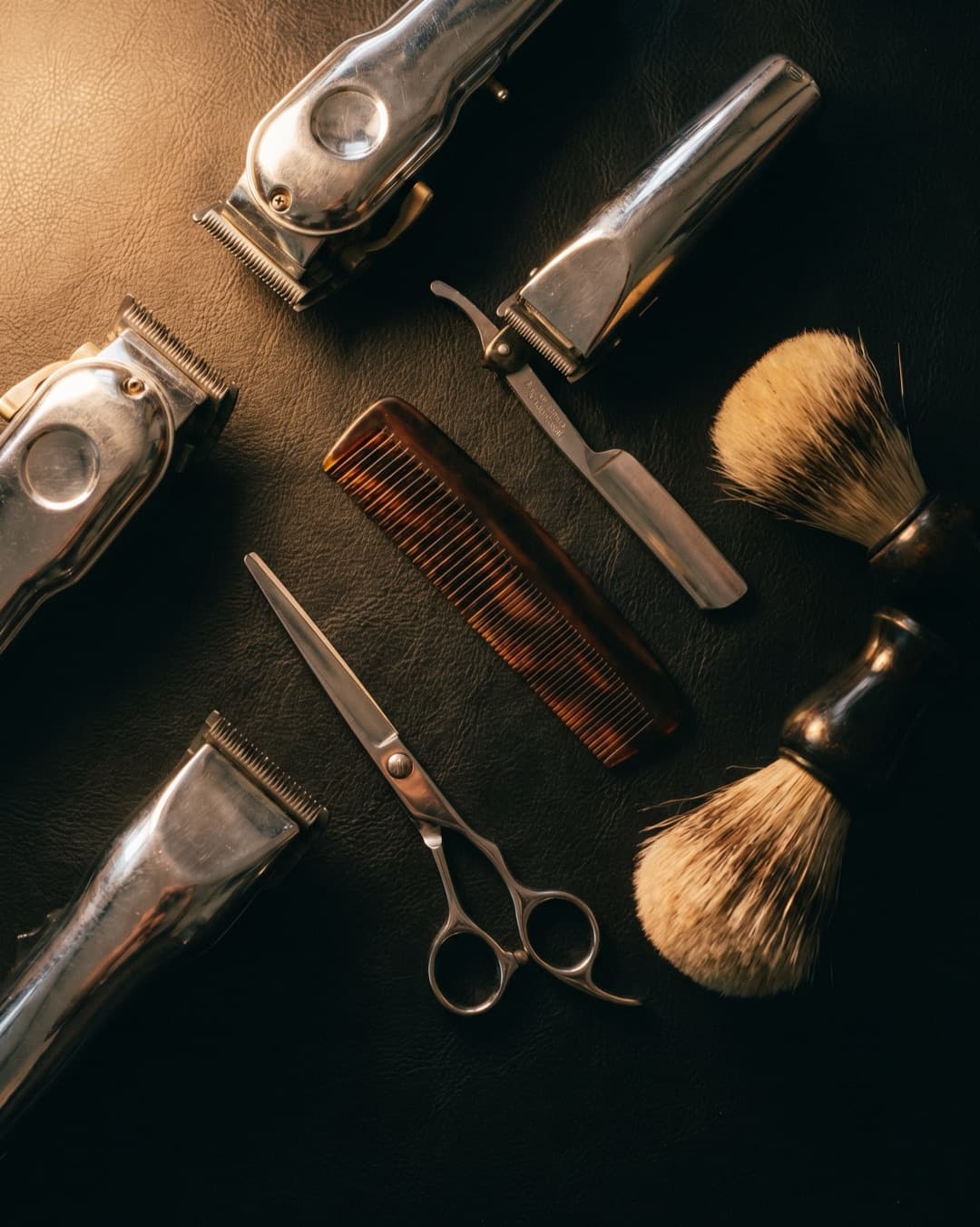 Clippers, razors, scissors and brushes laid out on a dark counter